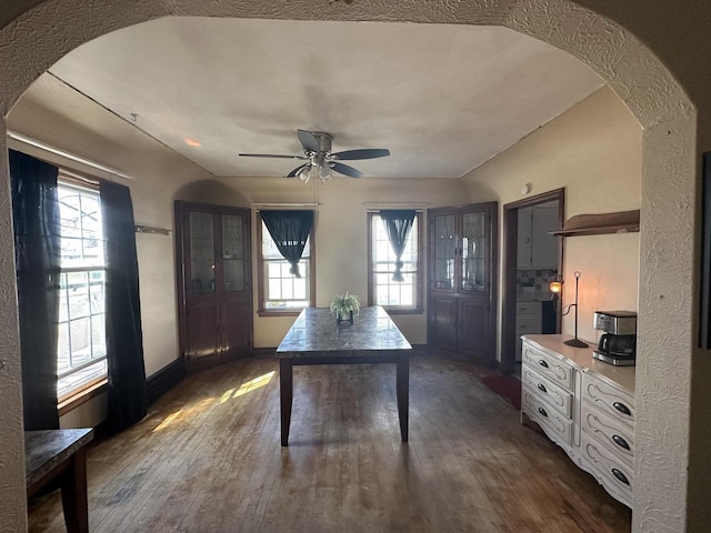 office area featuring arched walkways, dark wood finished floors, ceiling fan, and plenty of natural light