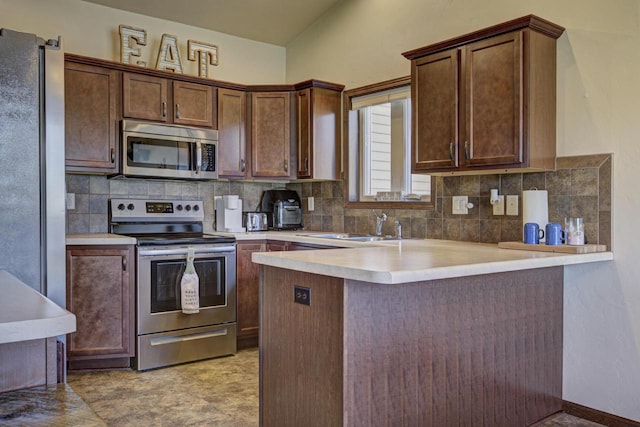 kitchen featuring stainless steel appliances, a sink, a peninsula, backsplash, and light countertops