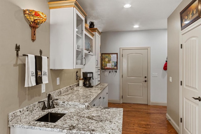 kitchen with glass insert cabinets, a sink, dark wood-type flooring, light stone counters, and recessed lighting