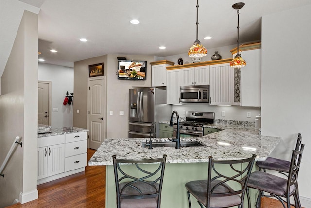 kitchen with light stone countertops, a sink, a peninsula, appliances with stainless steel finishes, and dark wood-style floors