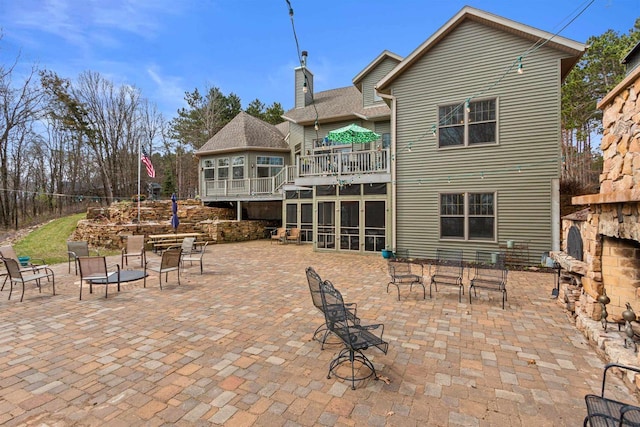 back of house with a chimney, a patio area, a sunroom, and a balcony