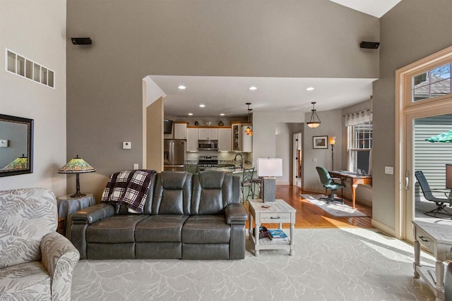 living room featuring recessed lighting, a high ceiling, visible vents, and light wood-style floors