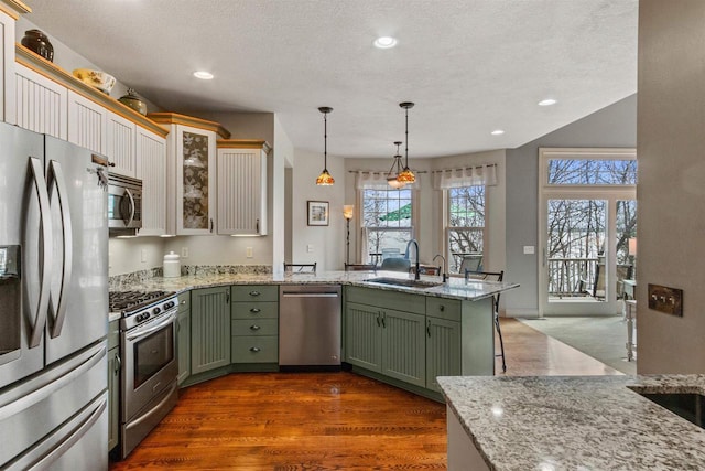 kitchen with a peninsula, a sink, green cabinets, appliances with stainless steel finishes, and light stone counters