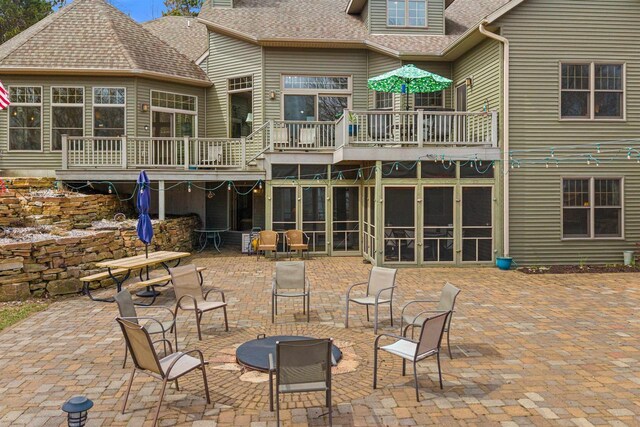 rear view of house with a balcony, roof with shingles, a patio, and a fire pit