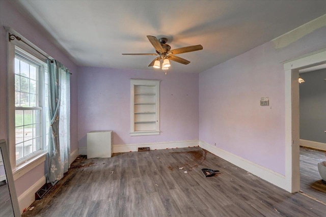 empty room with wood finished floors, plenty of natural light, built in shelves, and baseboards