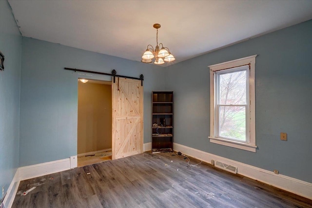 spare room with wood finished floors, a barn door, visible vents, a chandelier, and baseboards