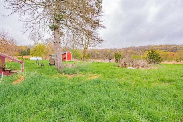 view of yard with a storage shed, a forest view, and an outbuilding