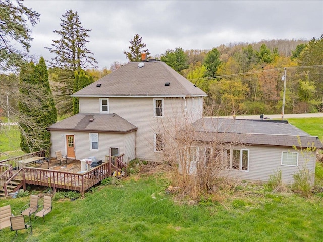 back of house with a lawn, a shingled roof, a forest view, and a wooden deck