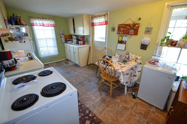 kitchen featuring a sink, white appliances, light countertops, stone finish flooring, and baseboards