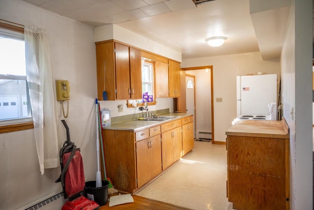 kitchen with a sink, freestanding refrigerator, a baseboard radiator, and a wealth of natural light