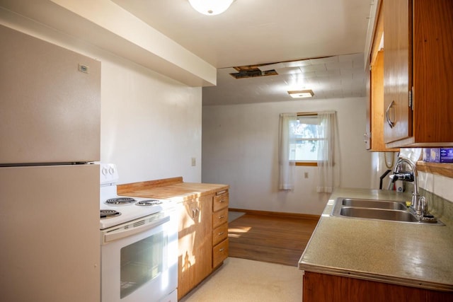 kitchen with brown cabinetry, baseboards, a sink, and white appliances