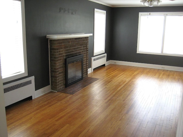 unfurnished living room featuring hardwood / wood-style flooring, a ceiling fan, a brick fireplace, and radiator heating unit