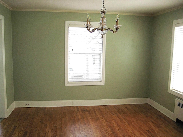 spare room with dark wood-style flooring, ornamental molding, a healthy amount of sunlight, and a chandelier