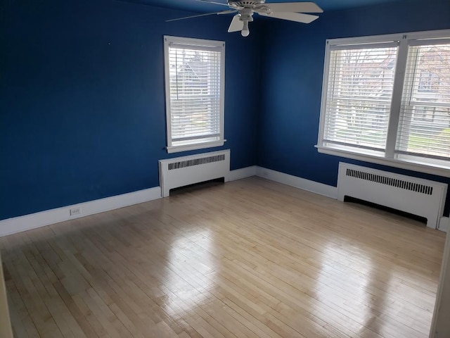 spare room featuring radiator, wood finished floors, baseboards, and a ceiling fan