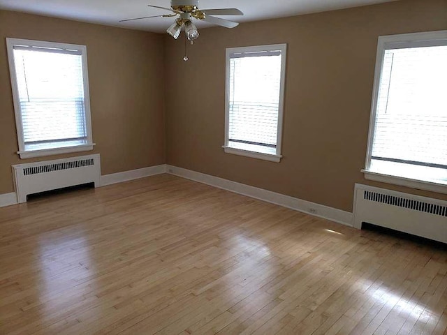 unfurnished room featuring radiator, light wood-style floors, a healthy amount of sunlight, and ceiling fan