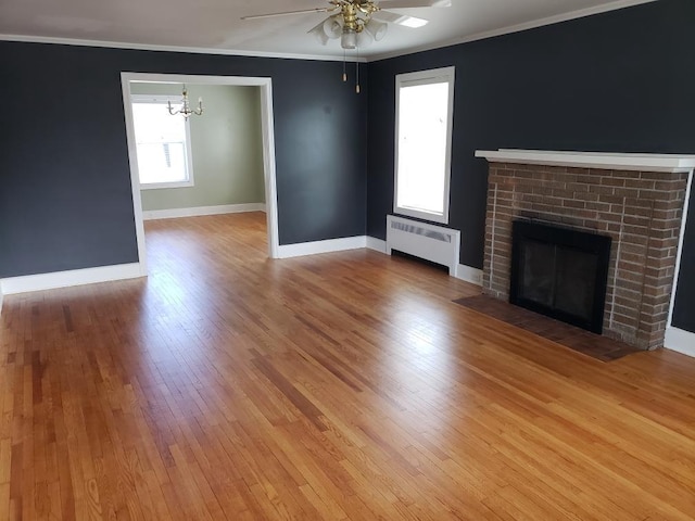 unfurnished living room with radiator, ceiling fan with notable chandelier, baseboards, and light wood-style floors
