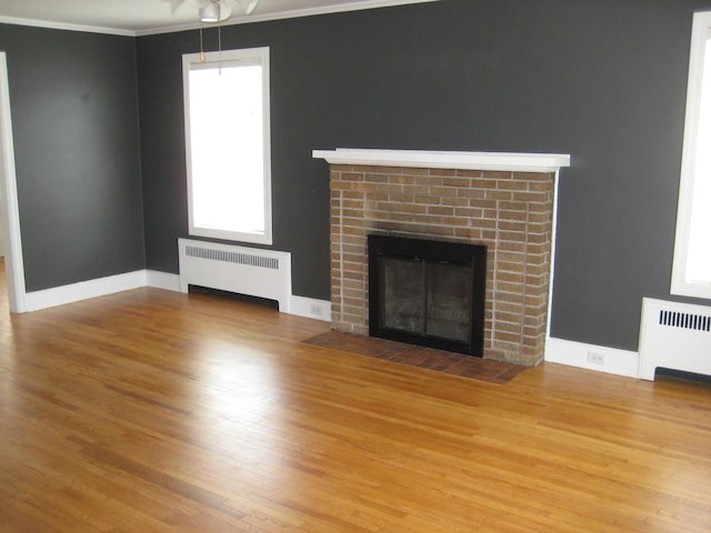 unfurnished living room with a fireplace, radiator, and wood finished floors