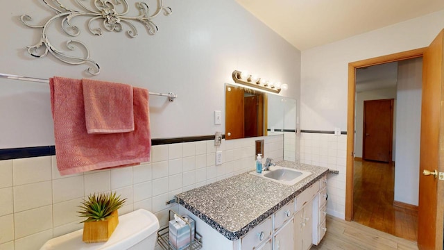 bathroom featuring tile walls, toilet, wood finished floors, vanity, and wainscoting