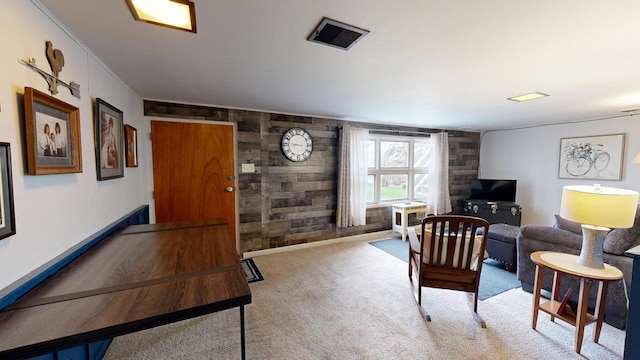 carpeted living area with wood walls, crown molding, and visible vents