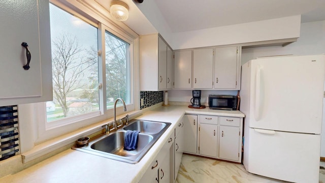 kitchen featuring a sink, freestanding refrigerator, stainless steel microwave, light countertops, and marble finish floor