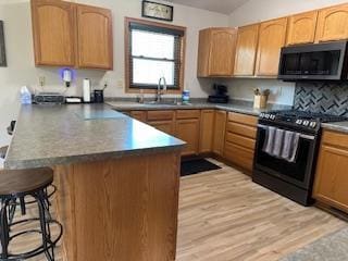 kitchen with a peninsula, a kitchen bar, a sink, stainless steel microwave, and range with gas stovetop
