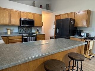 kitchen with a peninsula, light wood finished floors, a breakfast bar, appliances with stainless steel finishes, and decorative backsplash