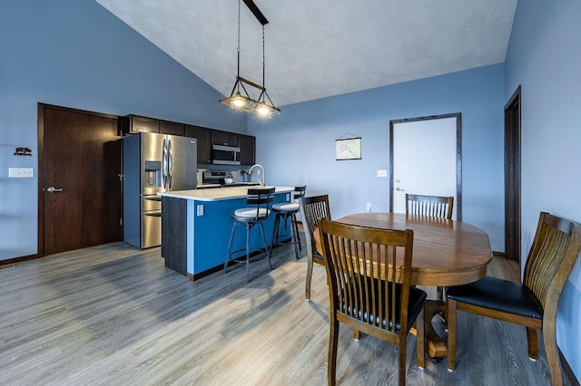 dining area with light wood-style flooring and high vaulted ceiling