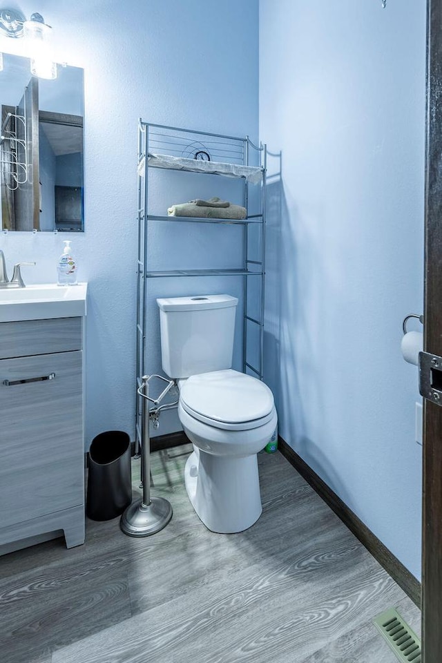 bathroom featuring toilet, wood finished floors, vanity, visible vents, and baseboards