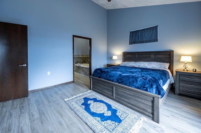bedroom with ensuite bathroom, wood finished floors, and baseboards
