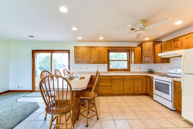 W10940 W Harmony Dr, Lodi, WI 53555 - kitchen with white appliances, under cabinet range hood, brown cabinets, light countertops, and a kitchen bar