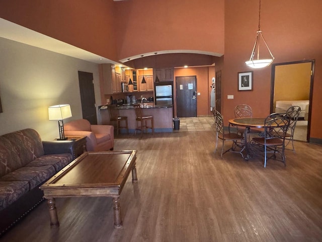 living room featuring a high ceiling, arched walkways, baseboards, and light wood-style floors