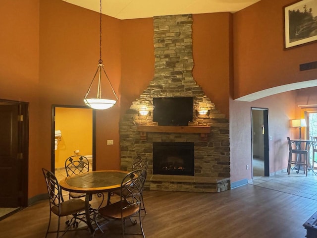 dining room with baseboards, visible vents, a towering ceiling, wood finished floors, and a fireplace