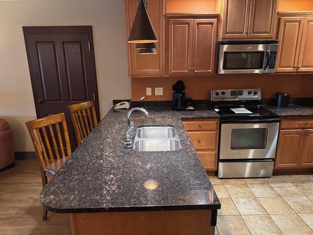 kitchen featuring a peninsula, brown cabinets, a sink, dark stone counters, and stainless steel appliances