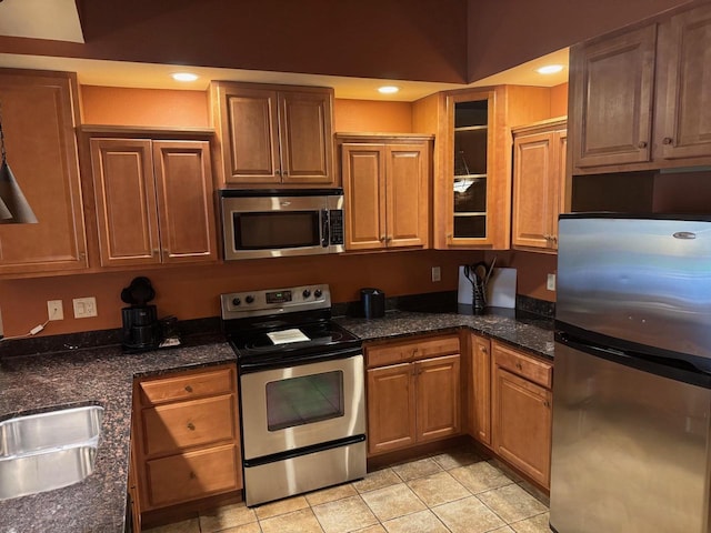 kitchen with a sink, stainless steel appliances, brown cabinets, light tile patterned flooring, and glass insert cabinets