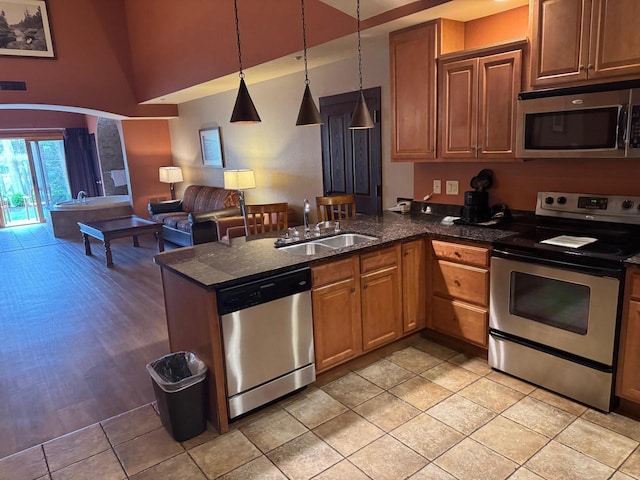kitchen with a peninsula, a sink, stainless steel appliances, pendant lighting, and open floor plan