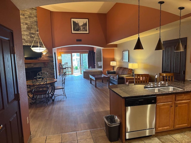 kitchen with a high ceiling, a sink, dark stone counters, a fireplace, and stainless steel dishwasher
