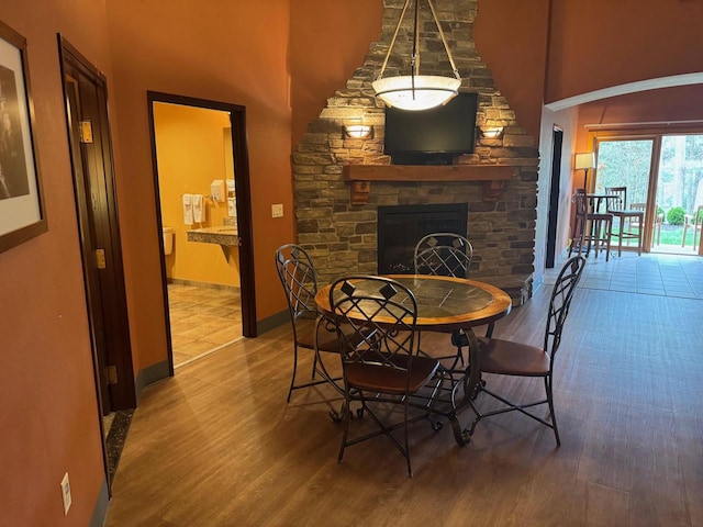 dining space featuring a towering ceiling, baseboards, a stone fireplace, and wood finished floors
