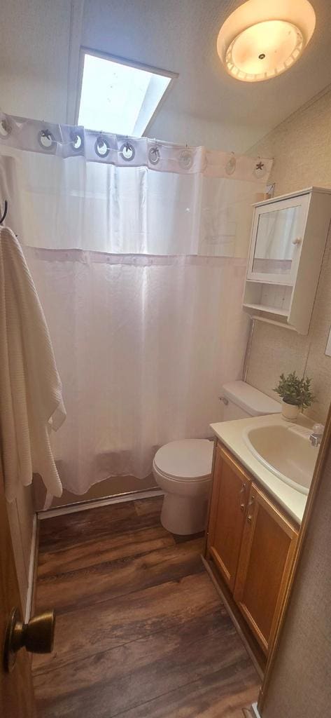 full bath with a shower with curtain, toilet, vanity, wood finished floors, and a skylight