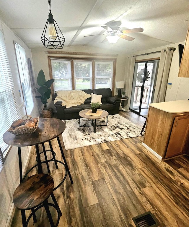 living area featuring a ceiling fan, lofted ceiling, visible vents, and wood finished floors