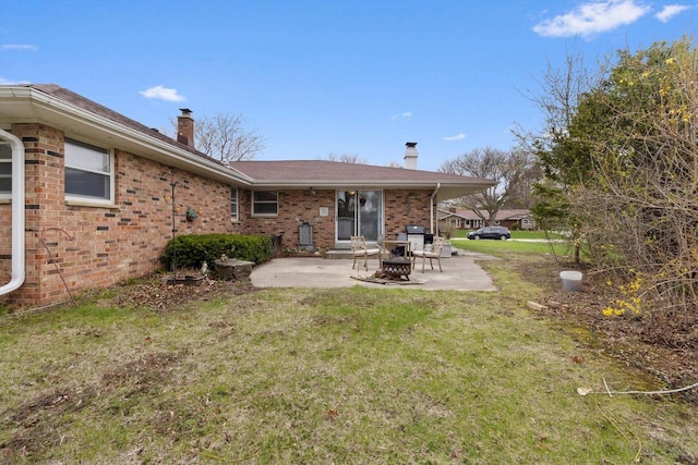 back of house featuring brick siding, a patio, a chimney, and a lawn