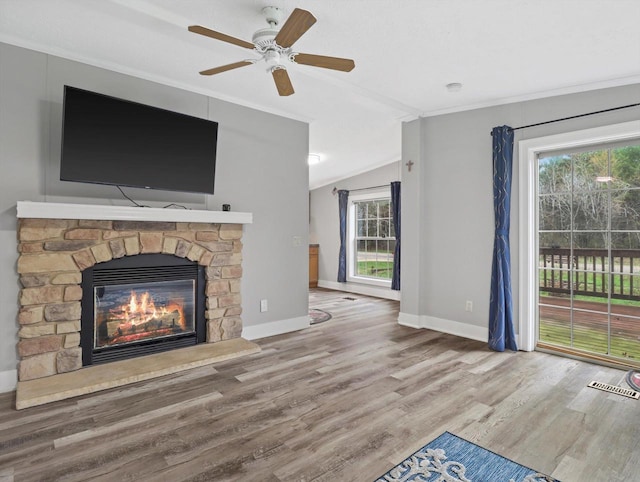 unfurnished living room featuring lofted ceiling, wood finished floors, ornamental molding, baseboards, and a stone fireplace