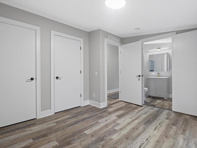 unfurnished bedroom with ensuite bath, wood finished floors, baseboards, and a sink