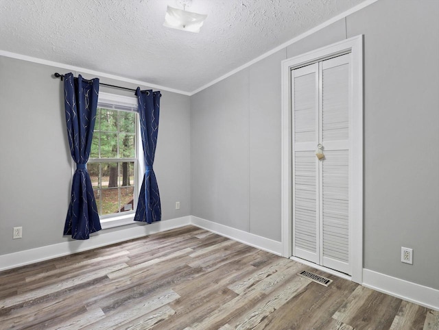 unfurnished bedroom featuring wood finished floors, a textured ceiling, visible vents, crown molding, and baseboards