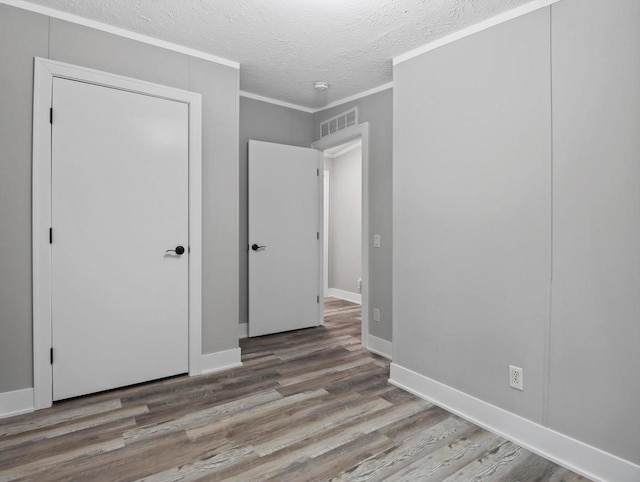 unfurnished bedroom with a textured ceiling, baseboards, visible vents, crown molding, and wood finished floors