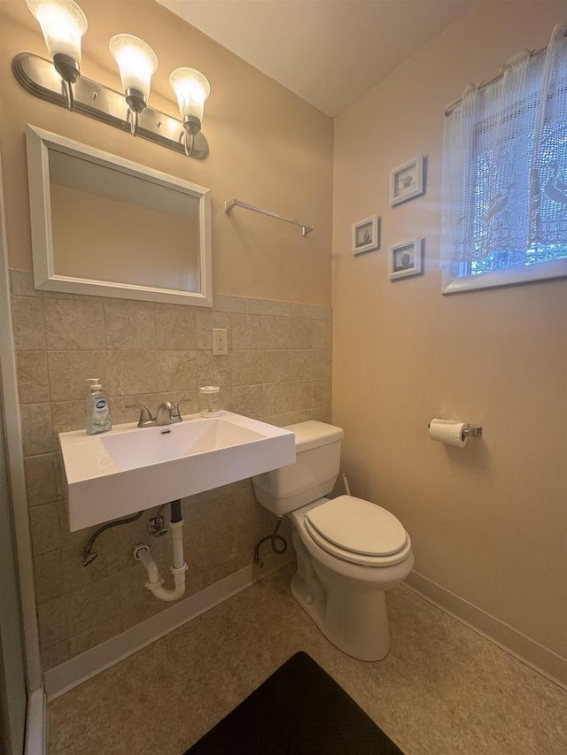 half bathroom featuring tile walls, toilet, and a sink
