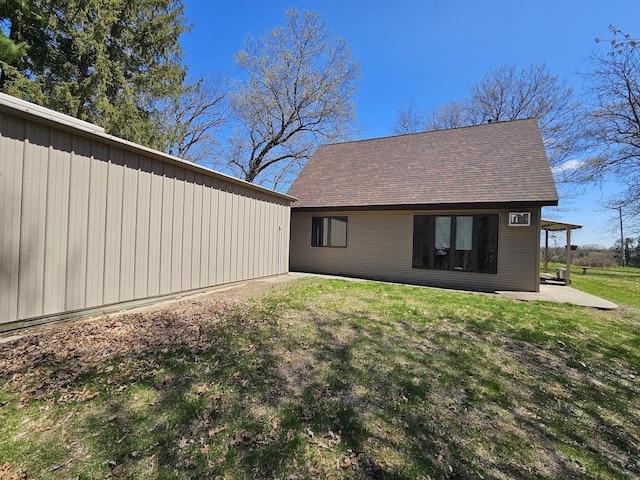 rear view of house with a lawn, a patio, and roof with shingles