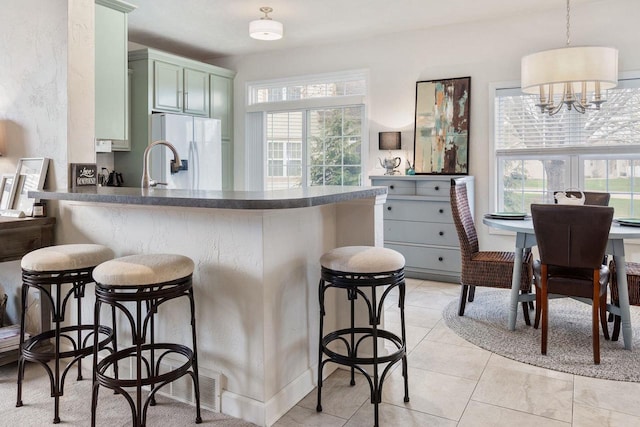 kitchen with a peninsula, green cabinetry, white fridge with ice dispenser, a breakfast bar area, and dark countertops