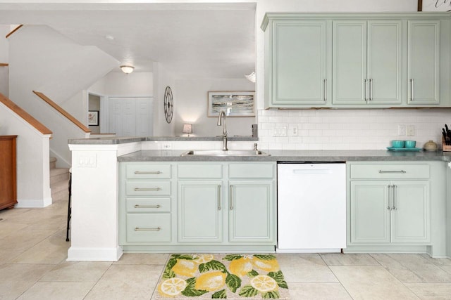 kitchen featuring dishwasher, light tile patterned floors, a sink, a peninsula, and backsplash