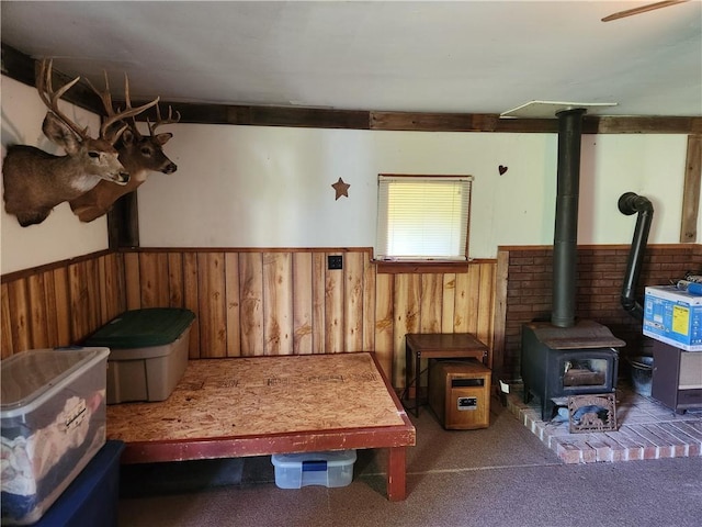 recreation room featuring a wood stove, wood walls, carpet floors, and a wainscoted wall