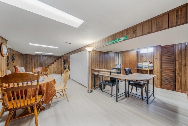 dining space featuring light wood finished floors, wooden walls, and stairs